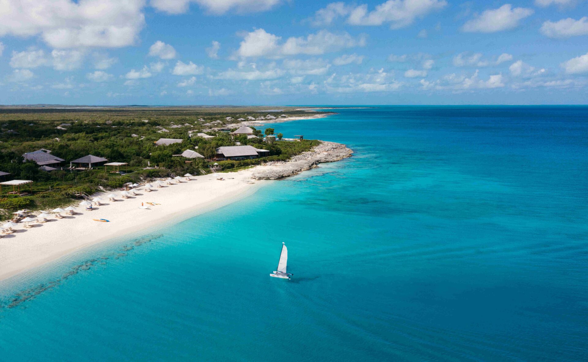 Aerial view of a Turks and Caicos beachfront resort with a catamaran sailing offshore
