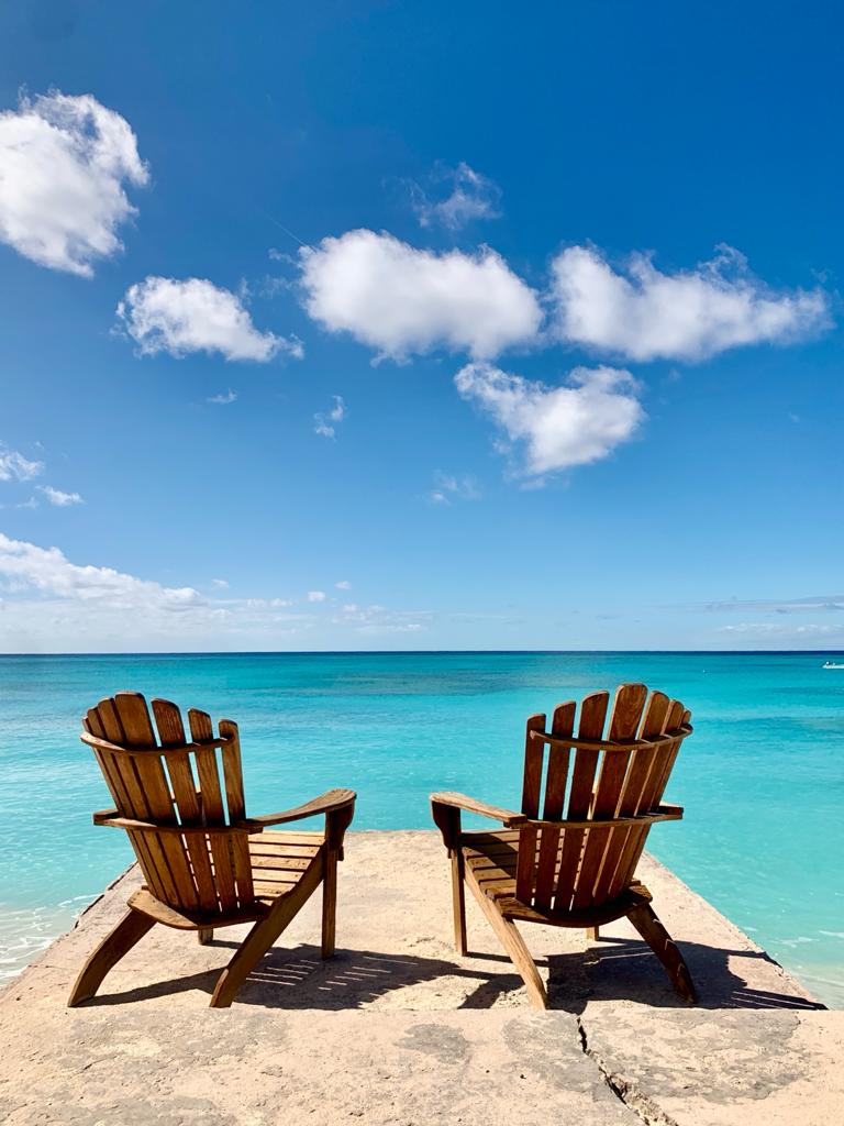 Two Adirondack chairs facing turquoise Turks and Caicos water under a blue sky
